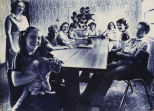 Eight women sit at a dining room table in a black and white photo from the 1970s.