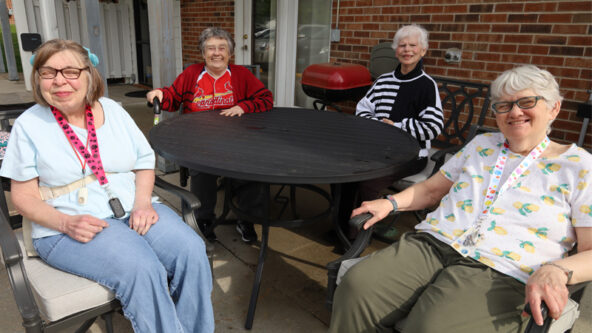 Carol, Betty, Jan, and Denise sit on the porch at their supported living site on a sunny day.