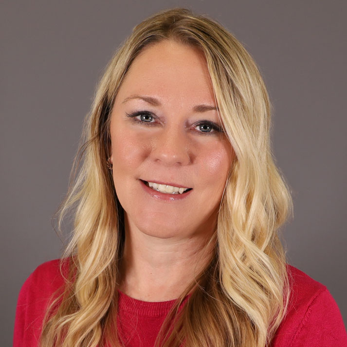 A light skin woman with long wavy blond hair. She is wearing a red sweater.