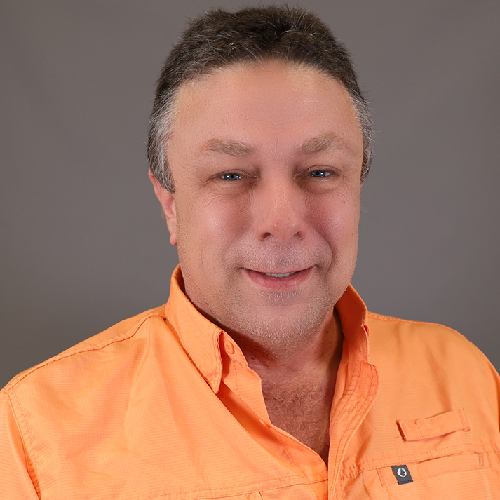 A light skin man with short dark grey hair. He is wearing a bright orange button up.