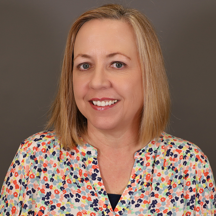 A light skin woman with shoulder length blonde hair, blue eyes wearing a brightly colored shirt.