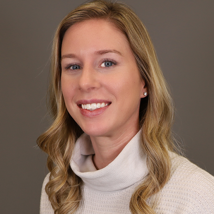 A light skin woman with long blonde-brown hair, blue eyes, is wearing a white turtleneck.